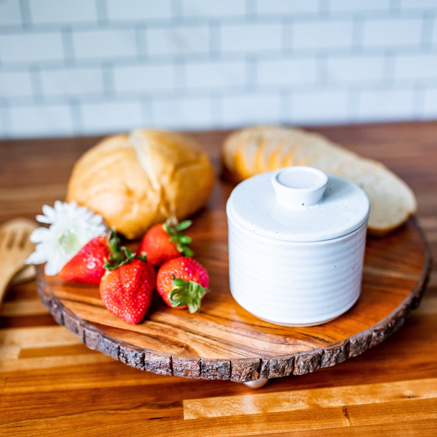 Wooden cutting board with strawberries, croissants, and a white butter crock on a wooden surface.
